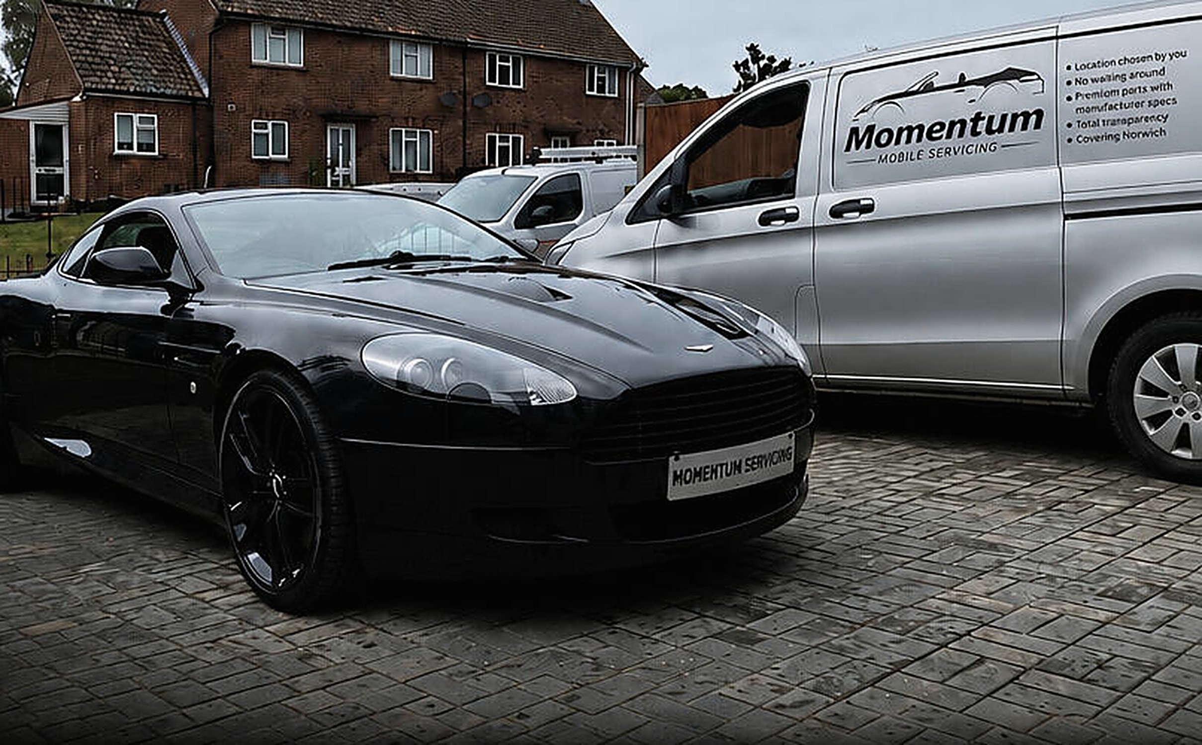 A black Aston Martin on a block-paved driveway beside the Momentum Mobile Servicing van